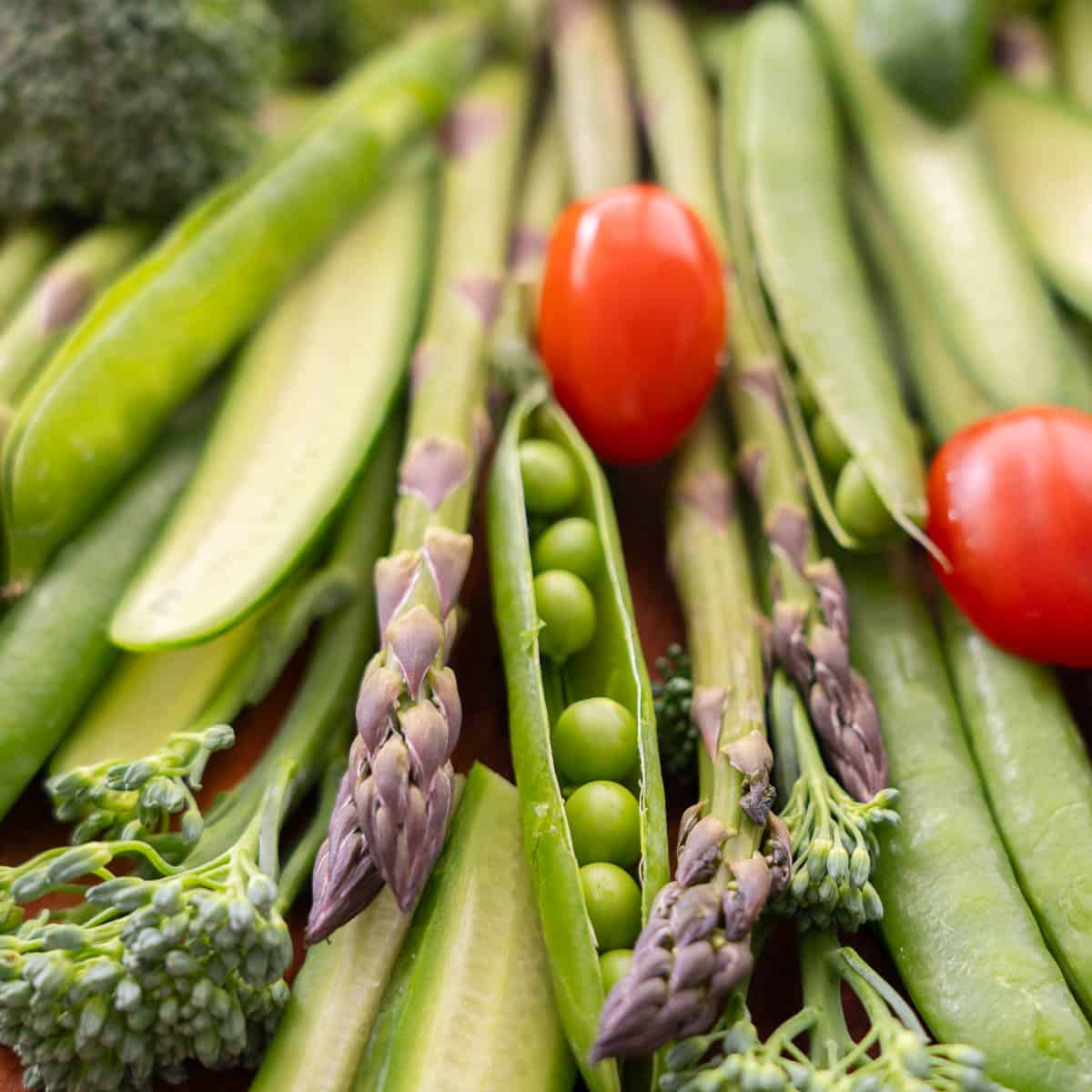 Close up of vegetables laid out on a wooden chopping board as a Christmas tree, cucumber slices, asparagus, broccolini, sweet peas as the branches and cherry tomatoes.