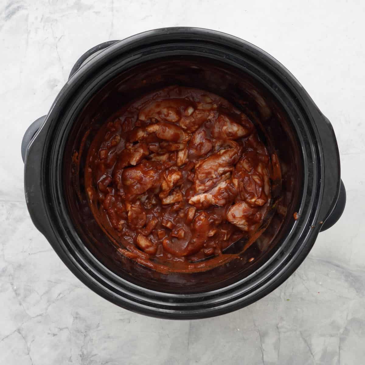 Chicken thighs added into diced onion, crushed garlic, tomato puree all the spices, brown sugar and cocoa powder in the bowl of crockpot.