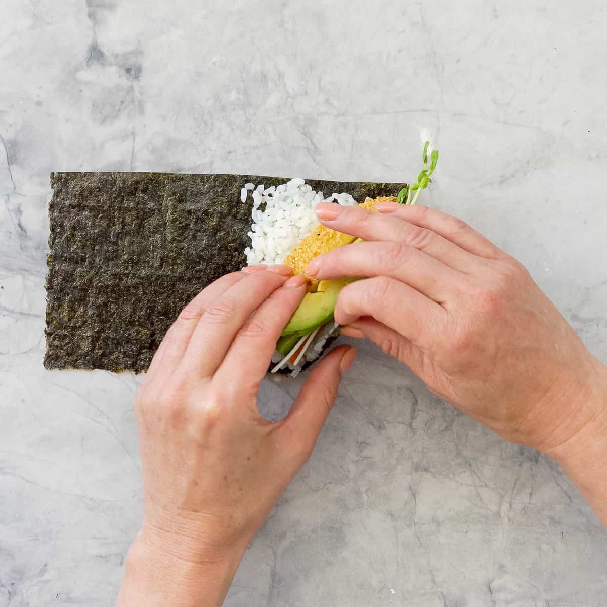 Nori, rice and fillings being rolled into a hand roll. 