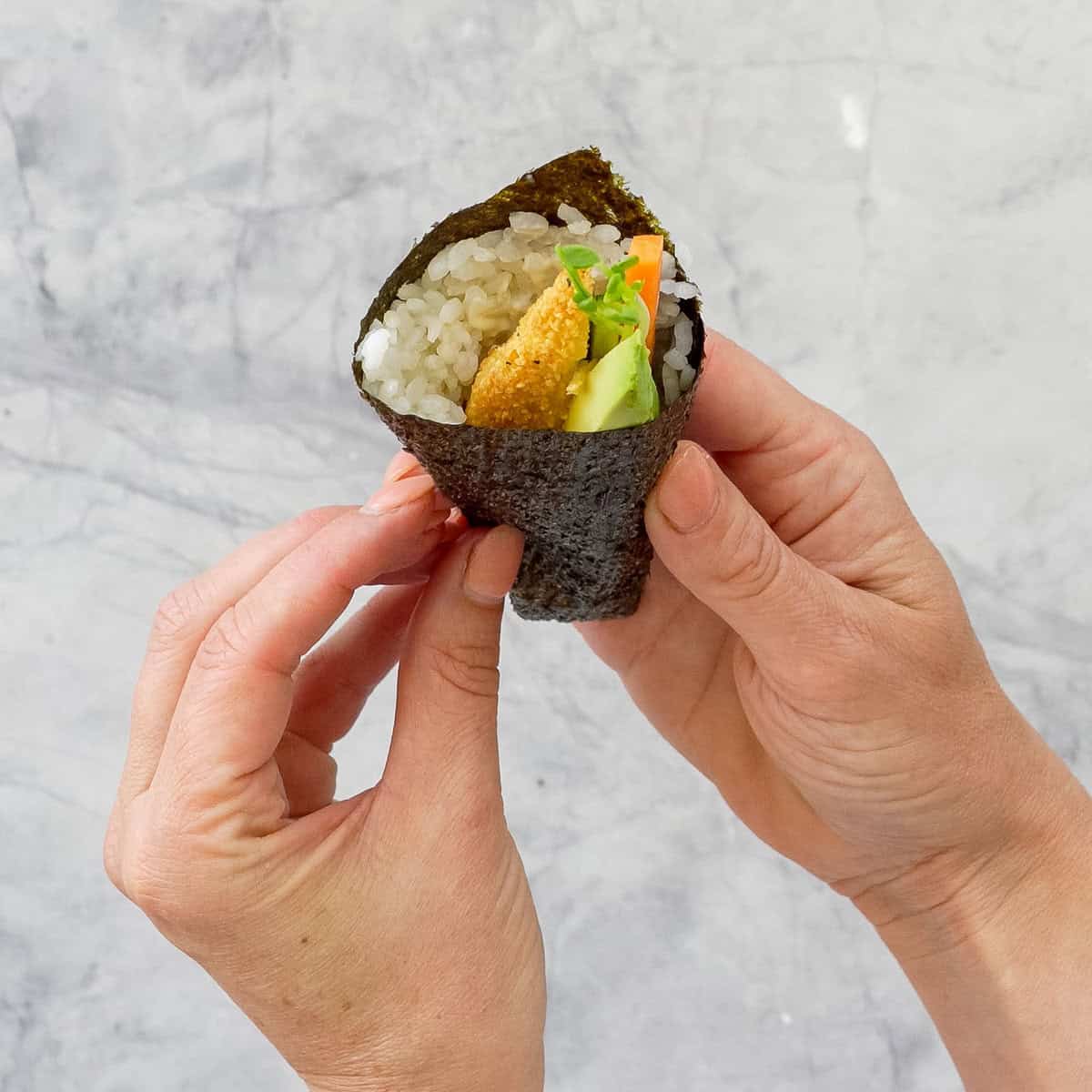 A hand roll sushi being held up to the camera. 