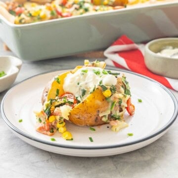 Loaded baked potato on a dinner plate garnished with toppings and sour cream.