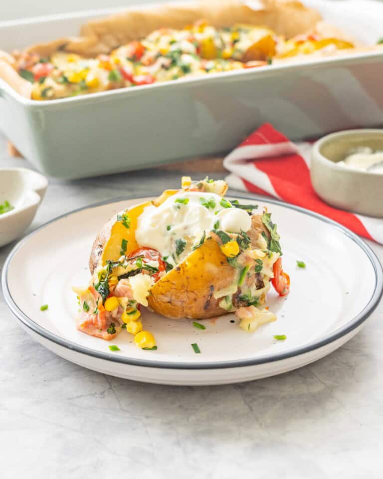 Loaded baked potato on a dinner plate garnished with toppings and sour cream.