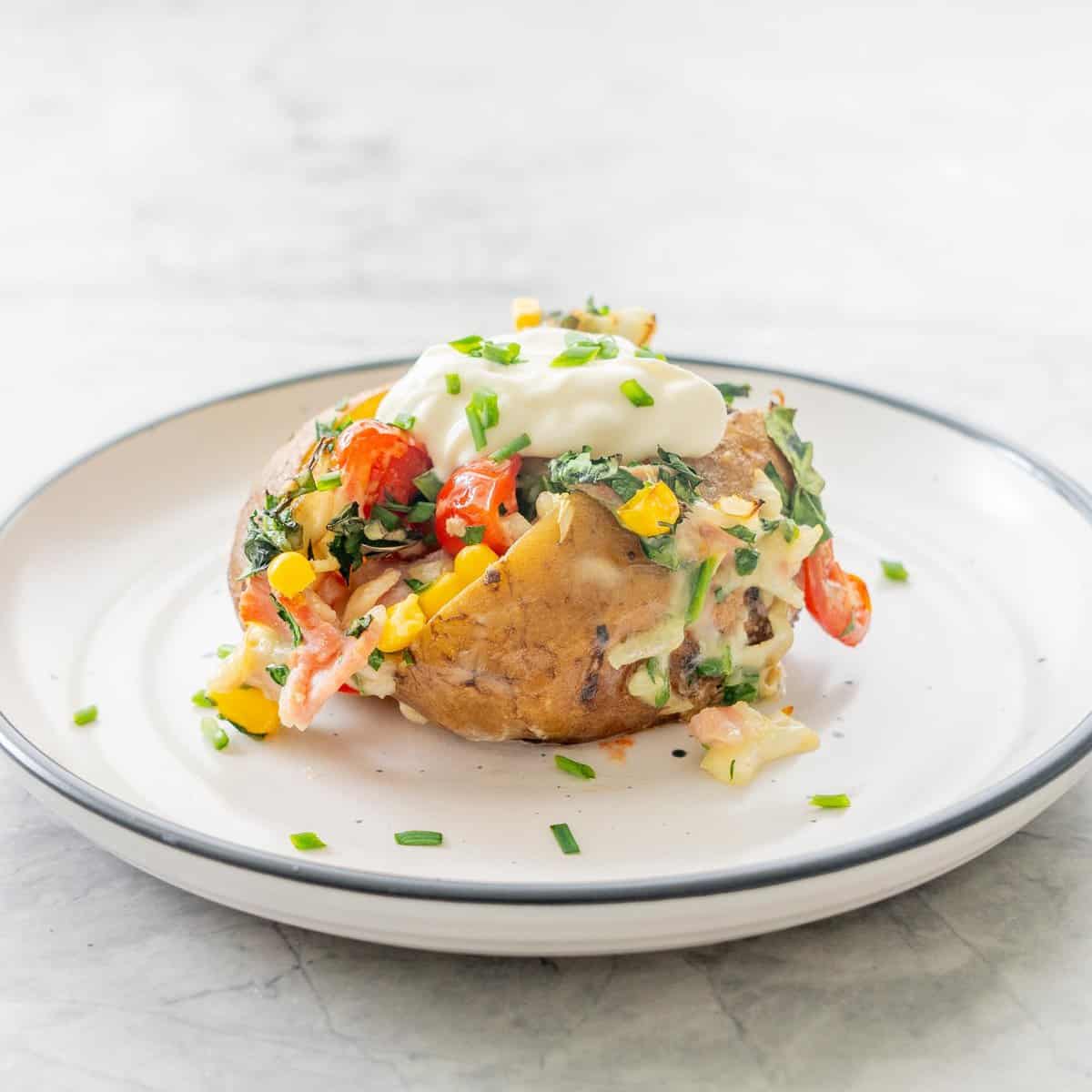 Loaded baked potato on a dinner plate garnished with toppings and sour cream.