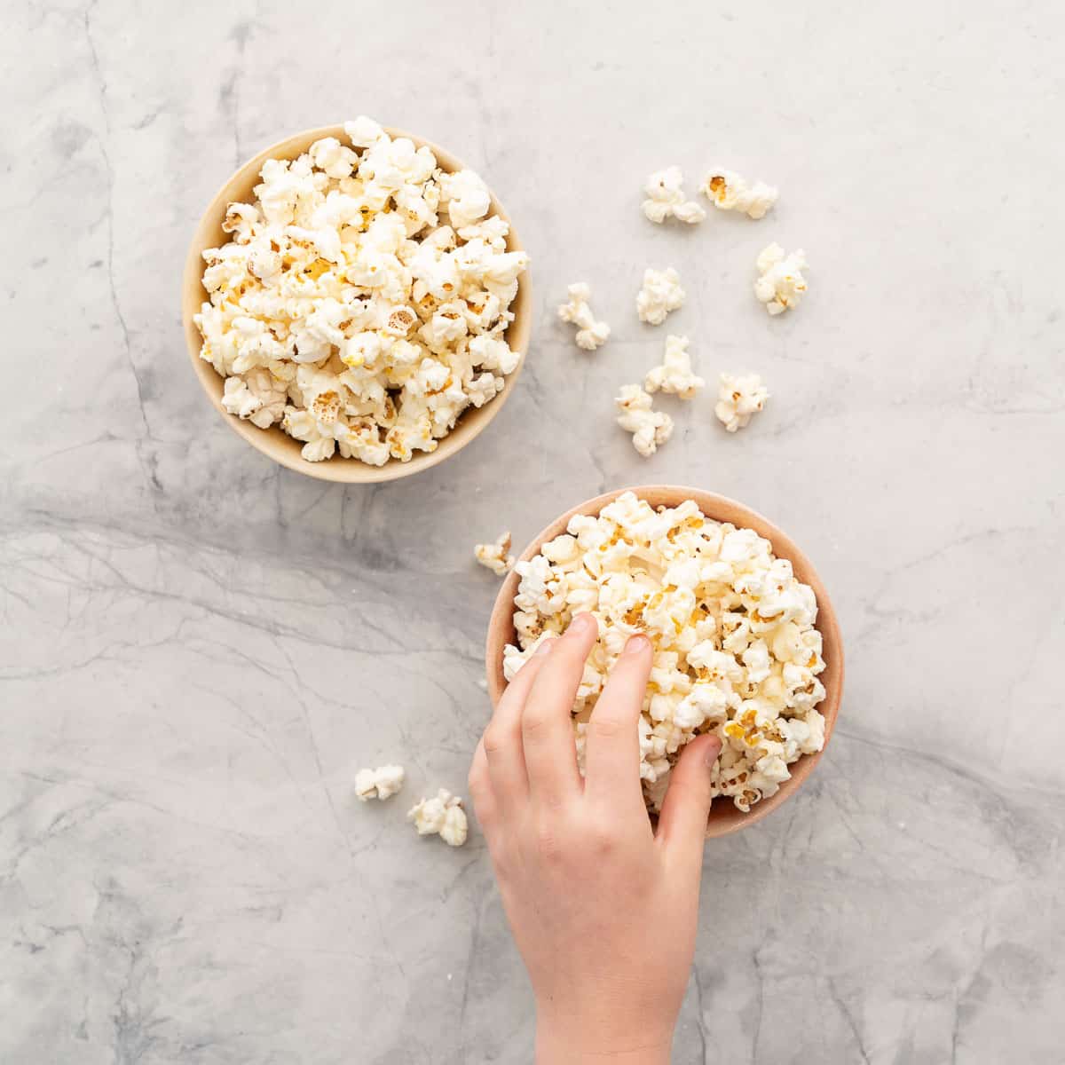 A hand reaching for popcorn from a pink ceramic bowl.