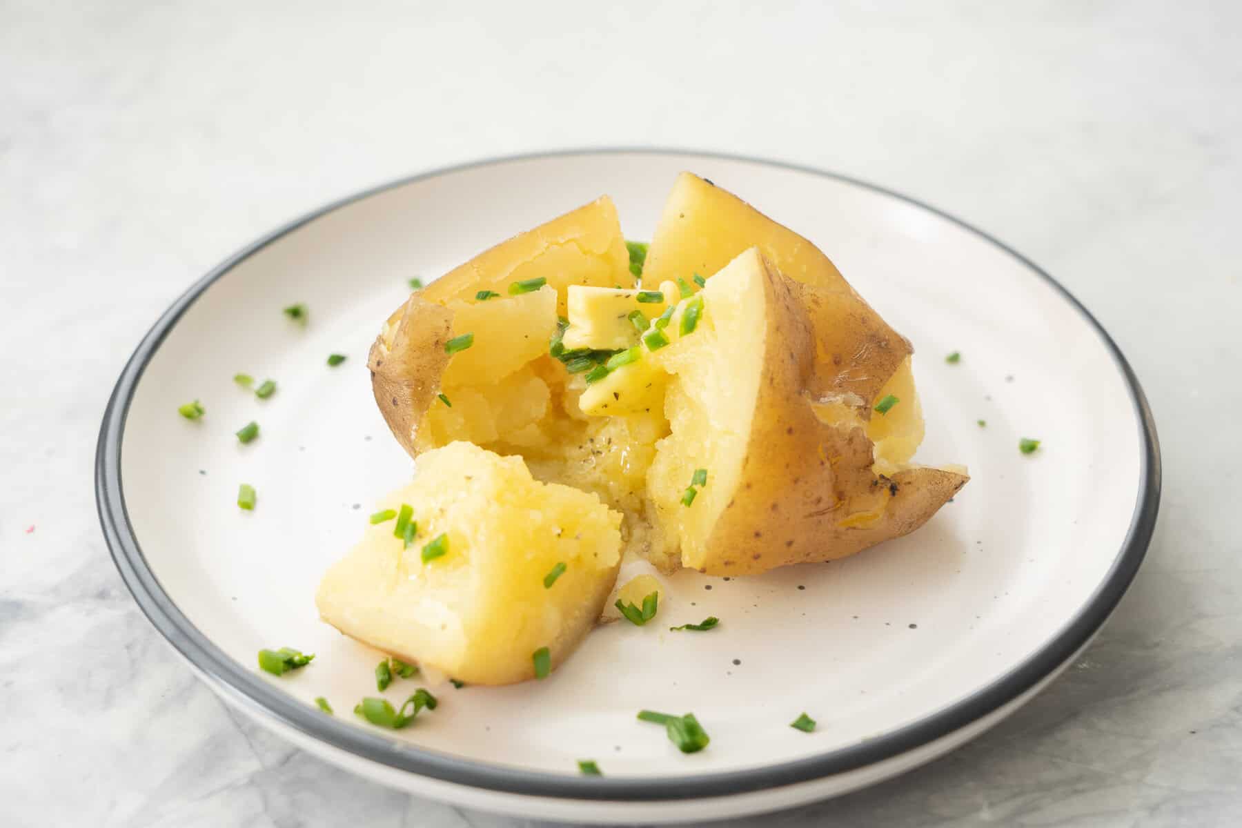 Slow cooker baked potato on a dinner plate cut in half with melted butter inside and sprinkled with chives.