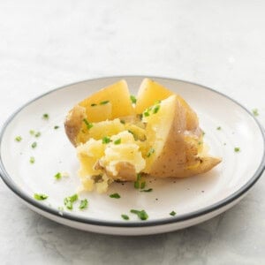 Slow cooker baked potato on a dinner plate cut in half with melted butter inside and sprinkled with chives.