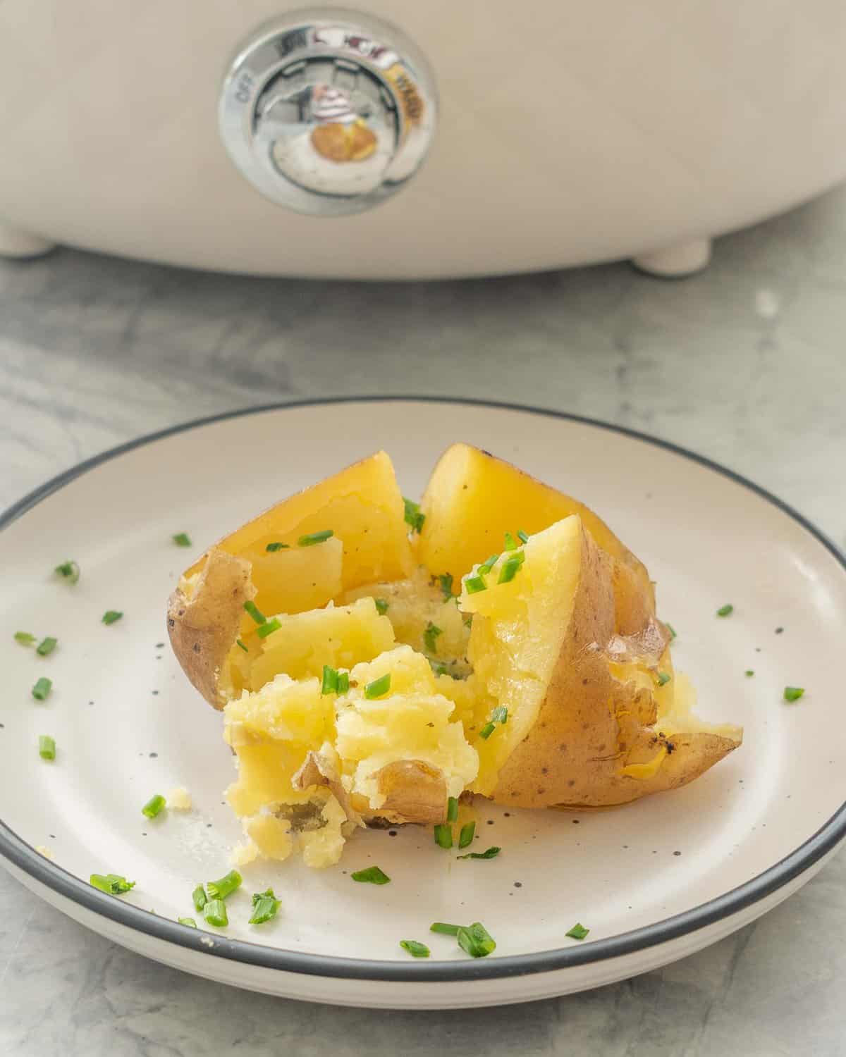 Slow cooker baked potato on a dinner plate cut in half with melted butter inside and sprinkled with chives.