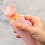 Hand holding a pink Popsicle holder with water and fruit ice block showing out of the top.