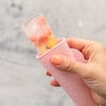 Hand holding a pink Popsicle holder with water and fruit ice block showing out of the top.
