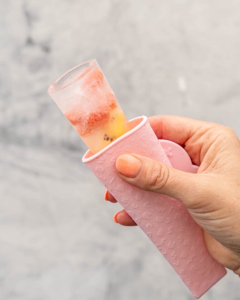 Hand holding a pink Popsicle holder with water and fruit ice block showing out of the top.