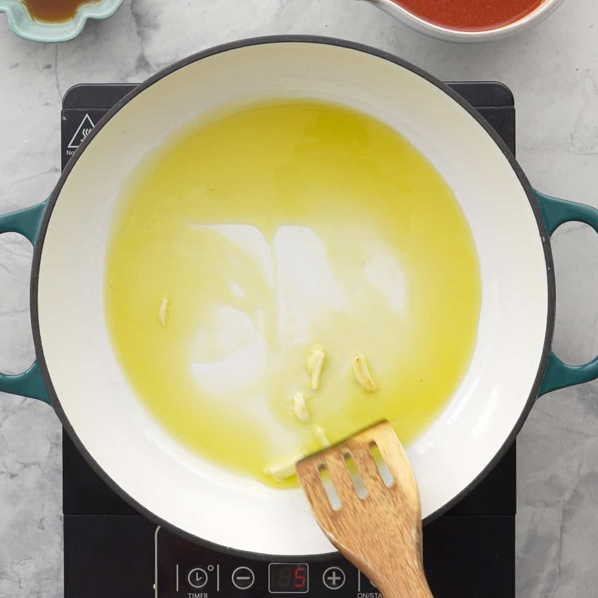 Oil and Garlic in a saucepan on stovetop with wooden spatula mixing.