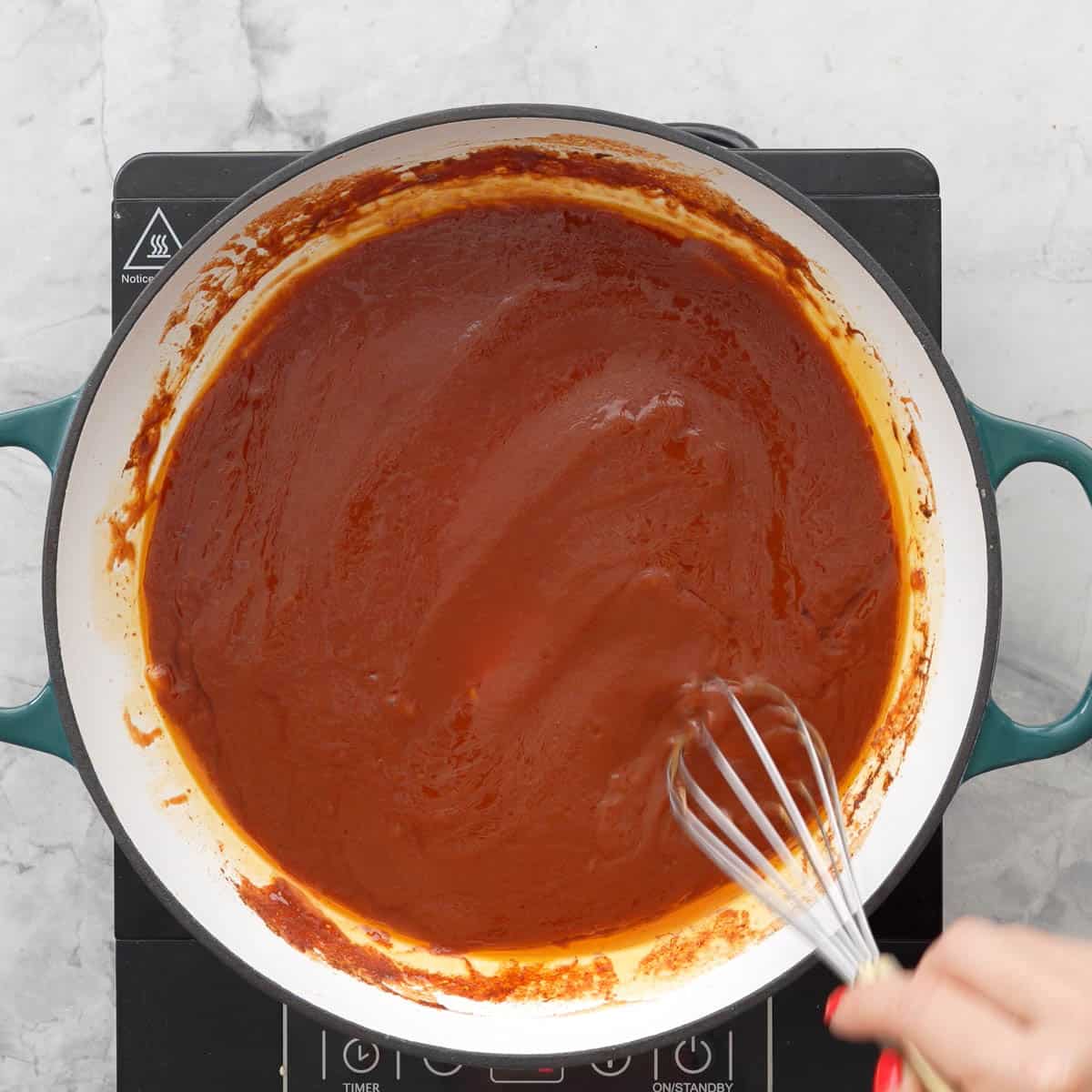 Whisk stirring together thickening tomato puree, cinnamon, maple syrup oil and garlic on stove top.