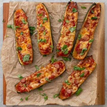 Cooked Zucchini Pizza boats laid on baking paper on wooden chopping board garnished with chopped basil.