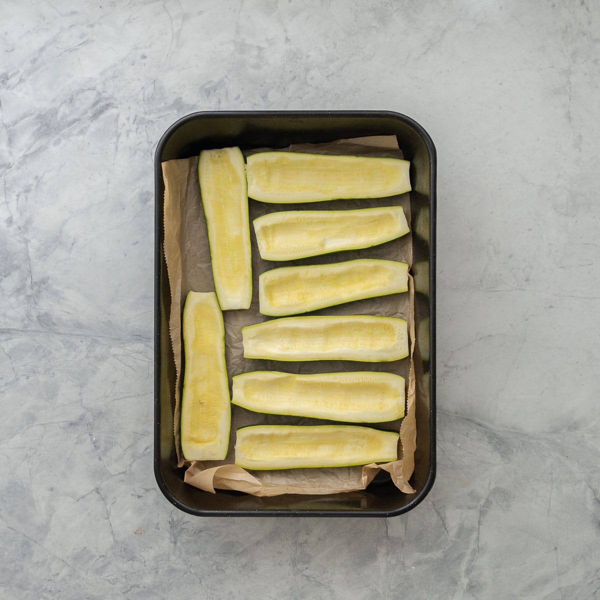 Eight hallowed out zucchini inside of a lined baking tray.