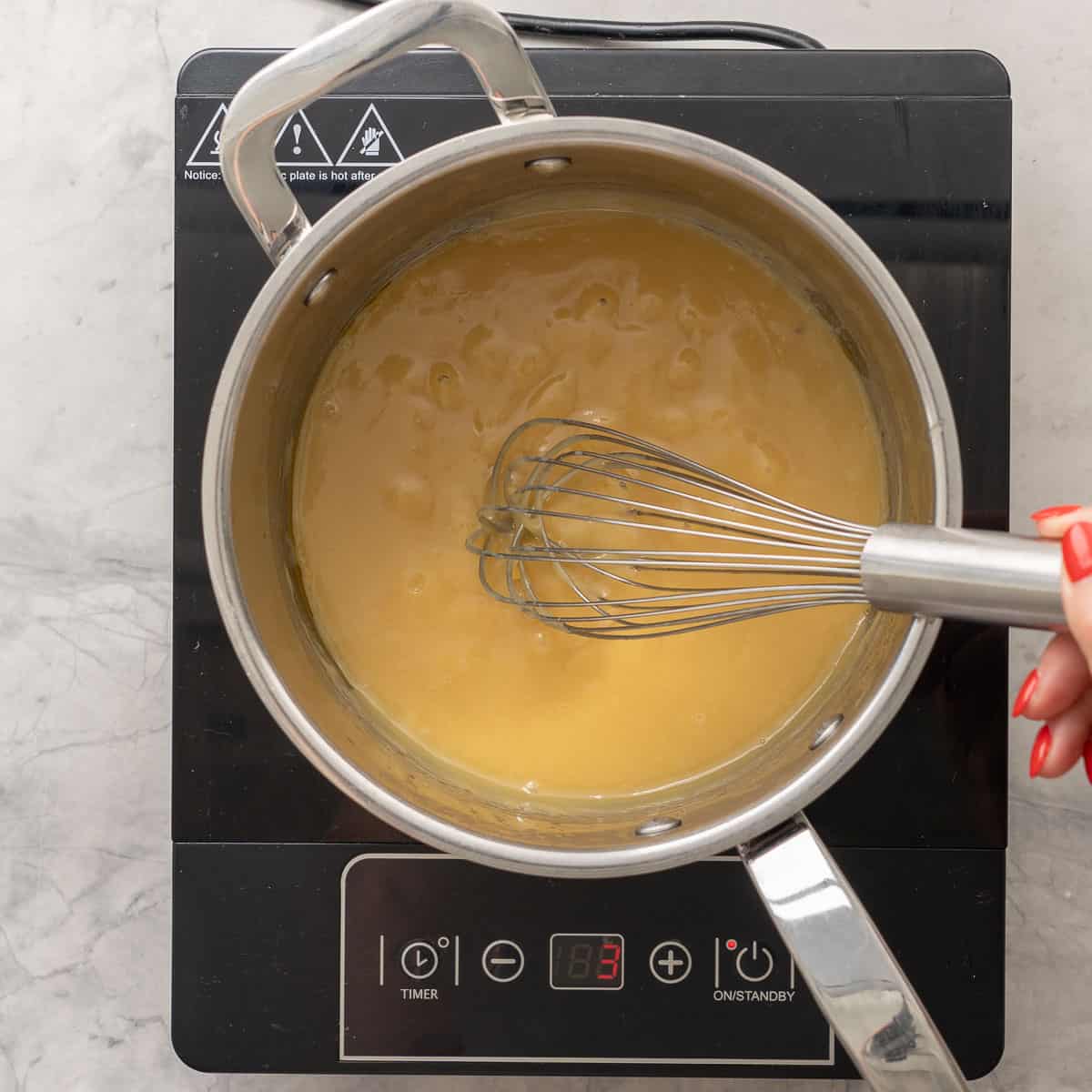 Hand holding a whisk stirring together butter, brown sugar, condense milk melting on stove top.