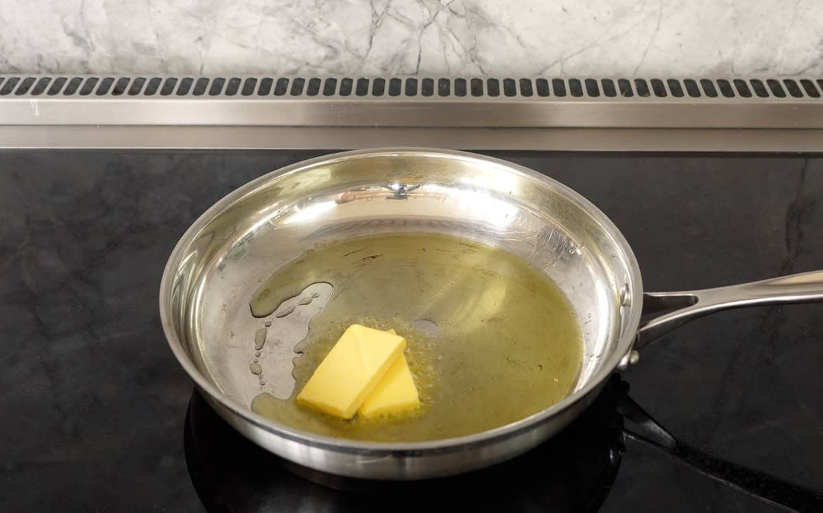 Two cubes of butter in frying pan melting on stove top.