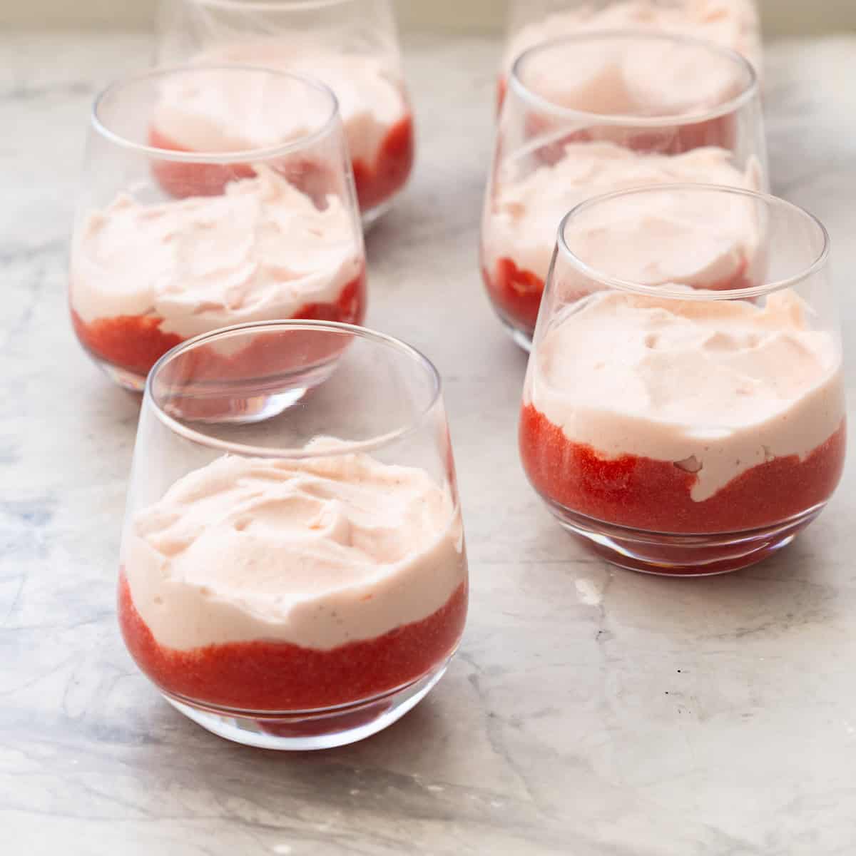 Six glasses of layered strawberry puree at base of glass with cream mixture layered on top.