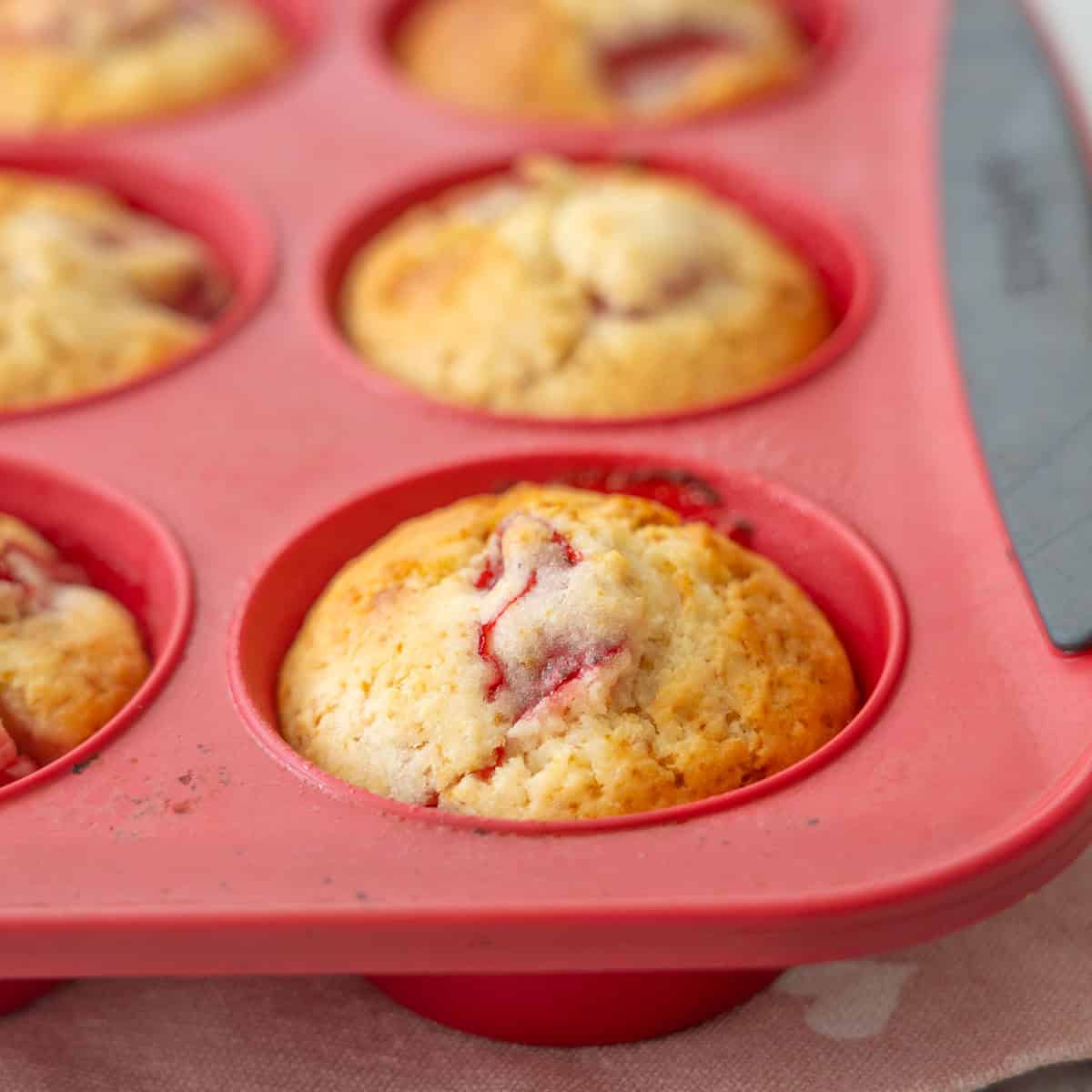 Close up of a cooked Strawberry muffin in red muffin tray.