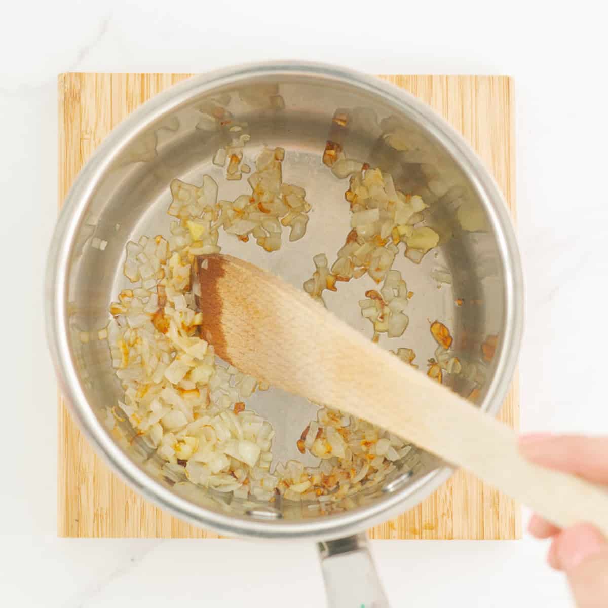 Onions sautéing in the bottom of a saucepan, being stirred with a wooden spoon.