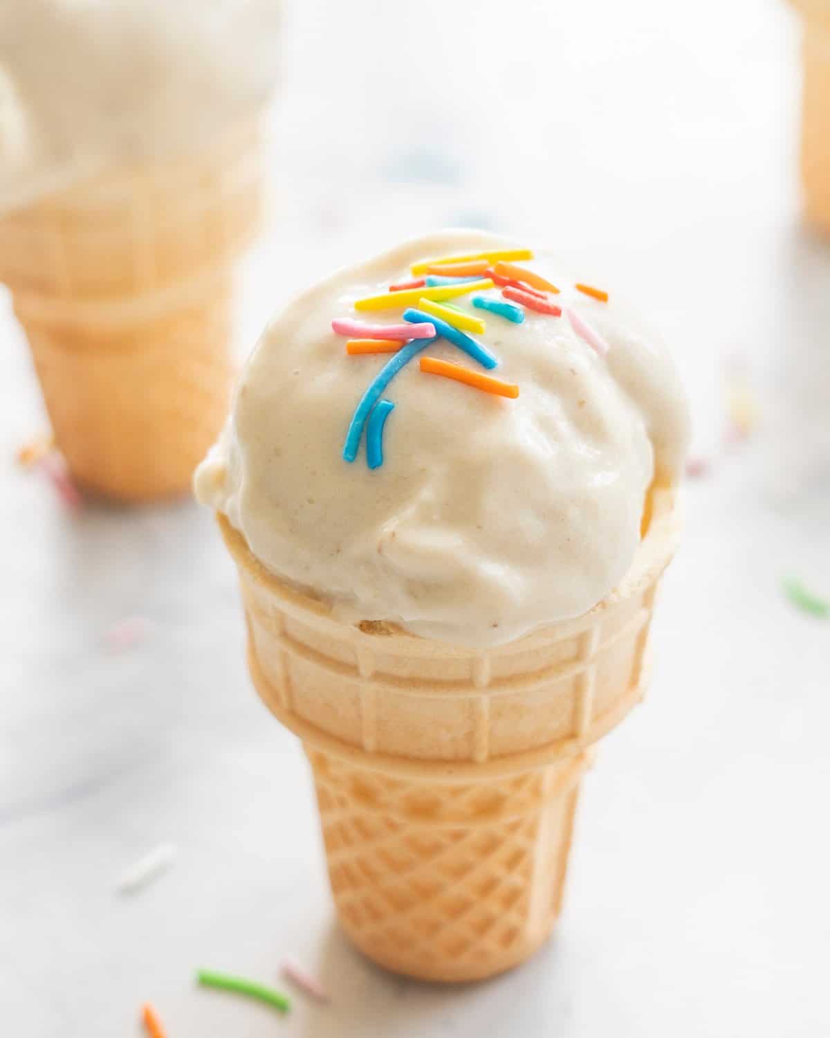 A mini ice cream cone on benchtop with Banana ice cream scooped on top, coloured sprinkles on top.