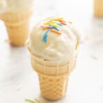A mini ice cream cone on benchtop with Banana ice cream scooped on top, coloured sprinkles on top.