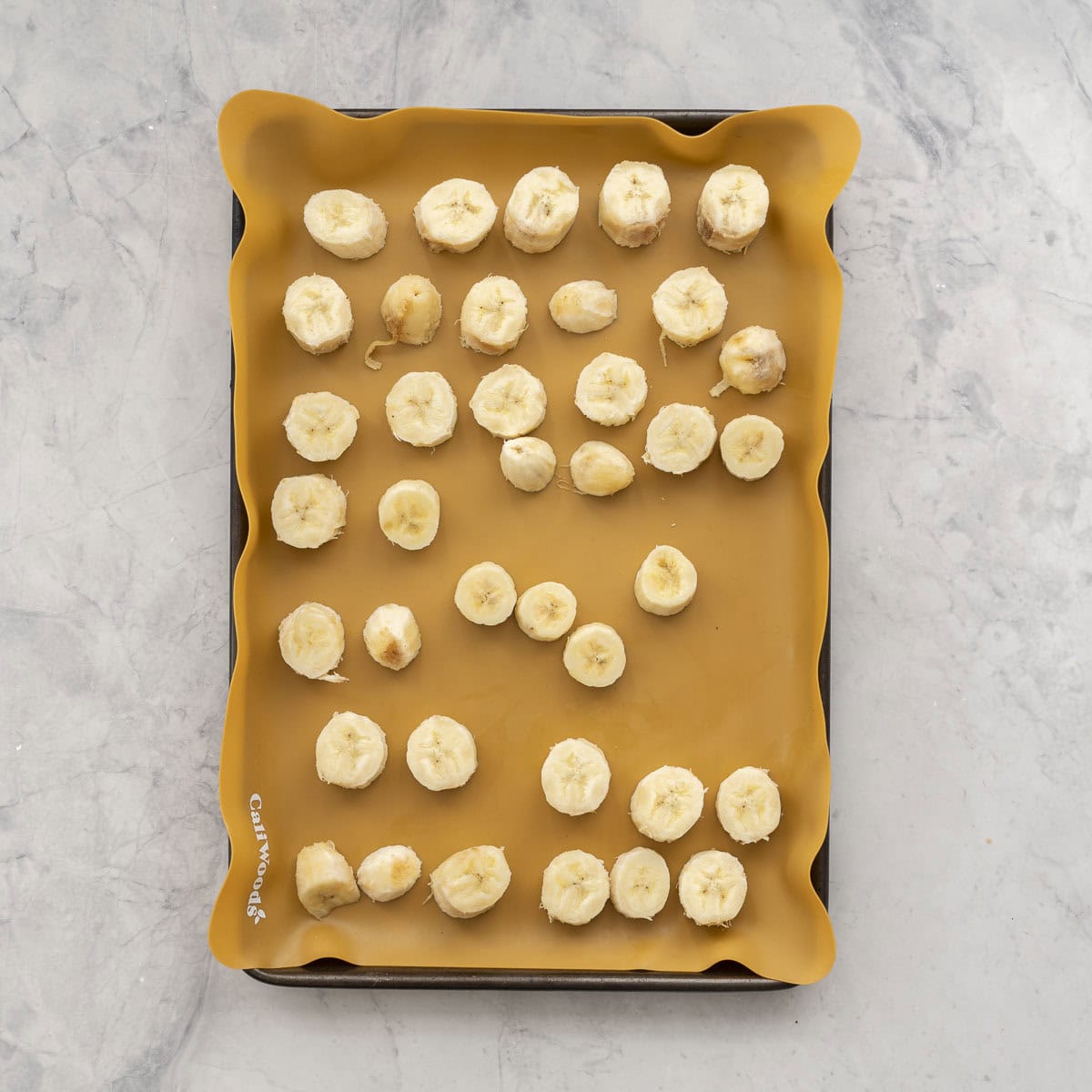 Banana slices laid on a silicone mat on tray on bench top.