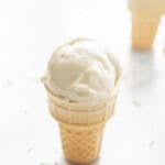 A mini ice cream cone on benchtop with Banana ice cream scooped on top, coloured sprinkles on bench.