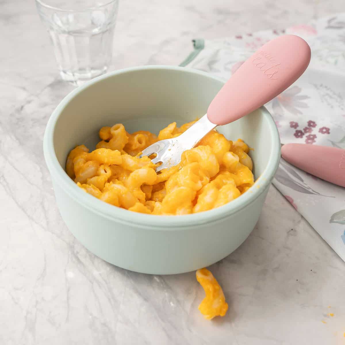 Silicone baby bowl with butternut mac and cheese inside, pink handled silicone toddler fork inside bowl.