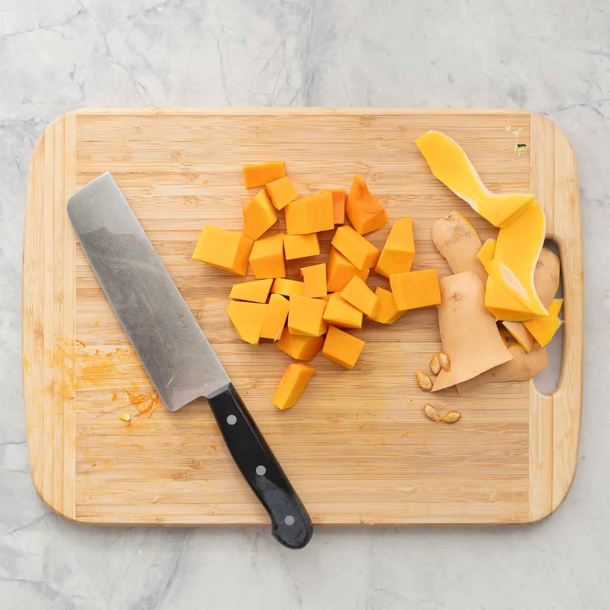 Butternut on wooden chopping board peeled and cut into rough cubes.