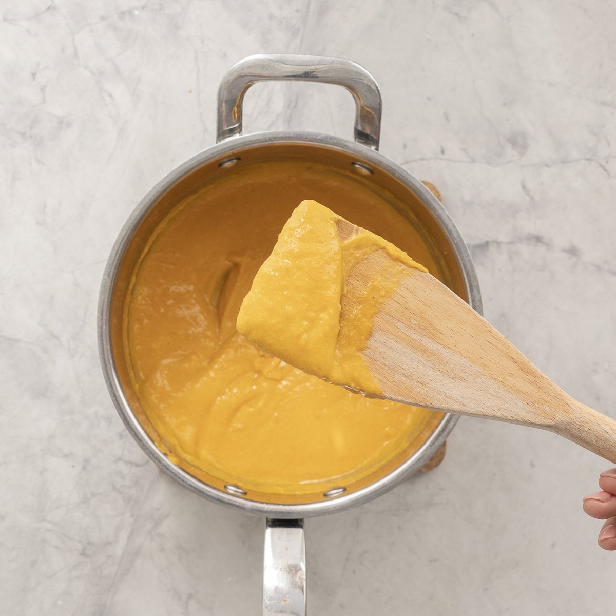 Wooden spoon with smooth butternut mixture held up above saucepan.