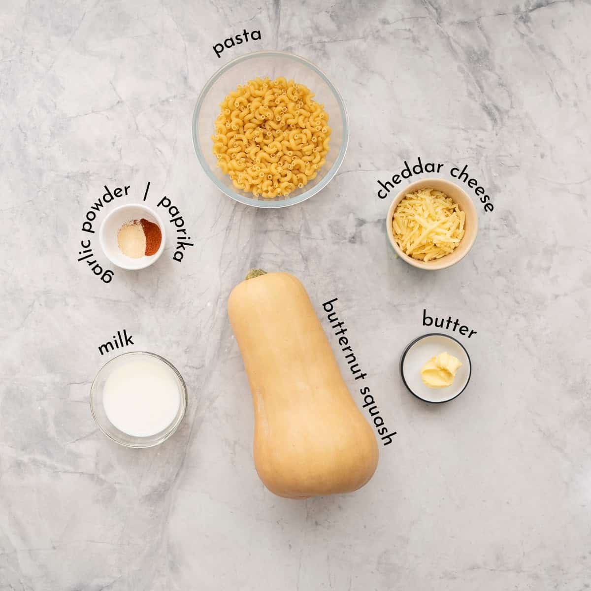 Ingredients for butternut squash mac and cheese on benchtop with text overlay.