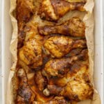 Nine cooked chicken drumsticks with sticky glossy paprika sauce on top inside a white oven dish lined with baking paper.