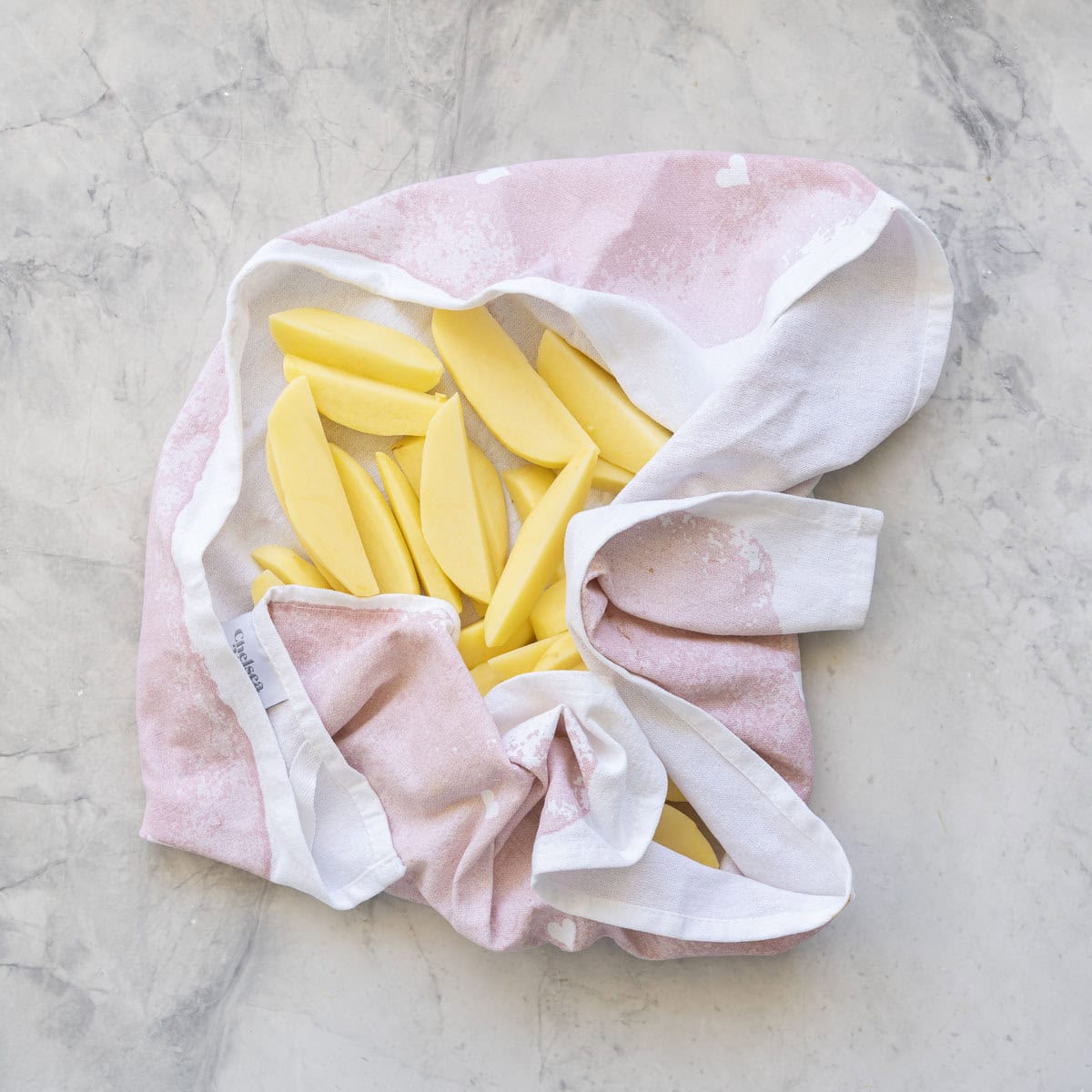 Potatoes chopped into wedges inside a tea towel on bench top.