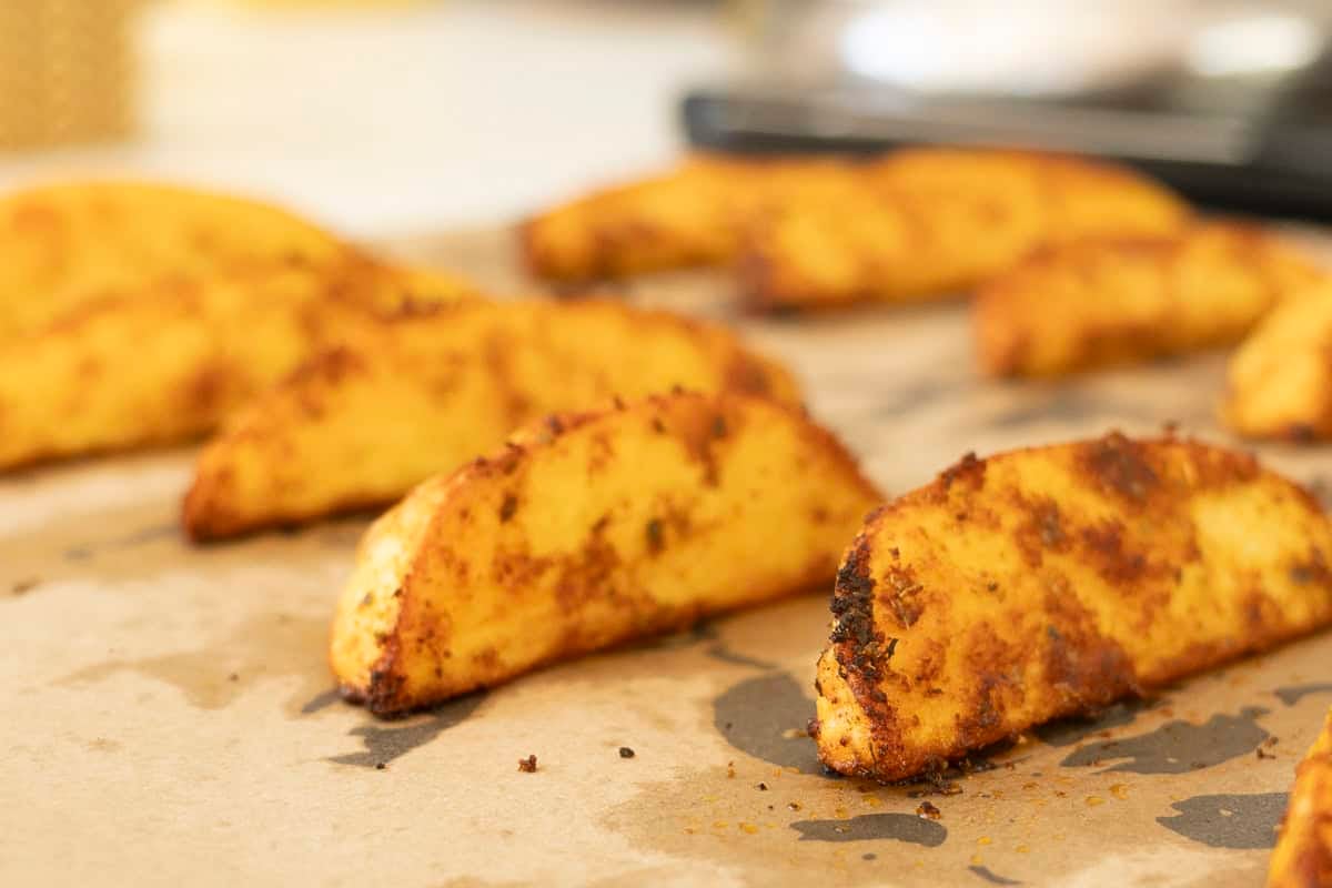 Crispy cooked potato wedges on baking tray lined with baking paper.