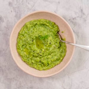 Mashed peas in a bowl with spoon garnished with piece of parsley and cracked pepper.