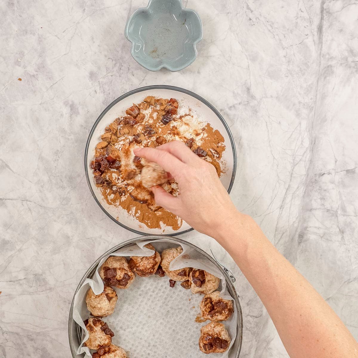 Hand holding a monkey bread ball rolling it in cinnamon mixture on plate.