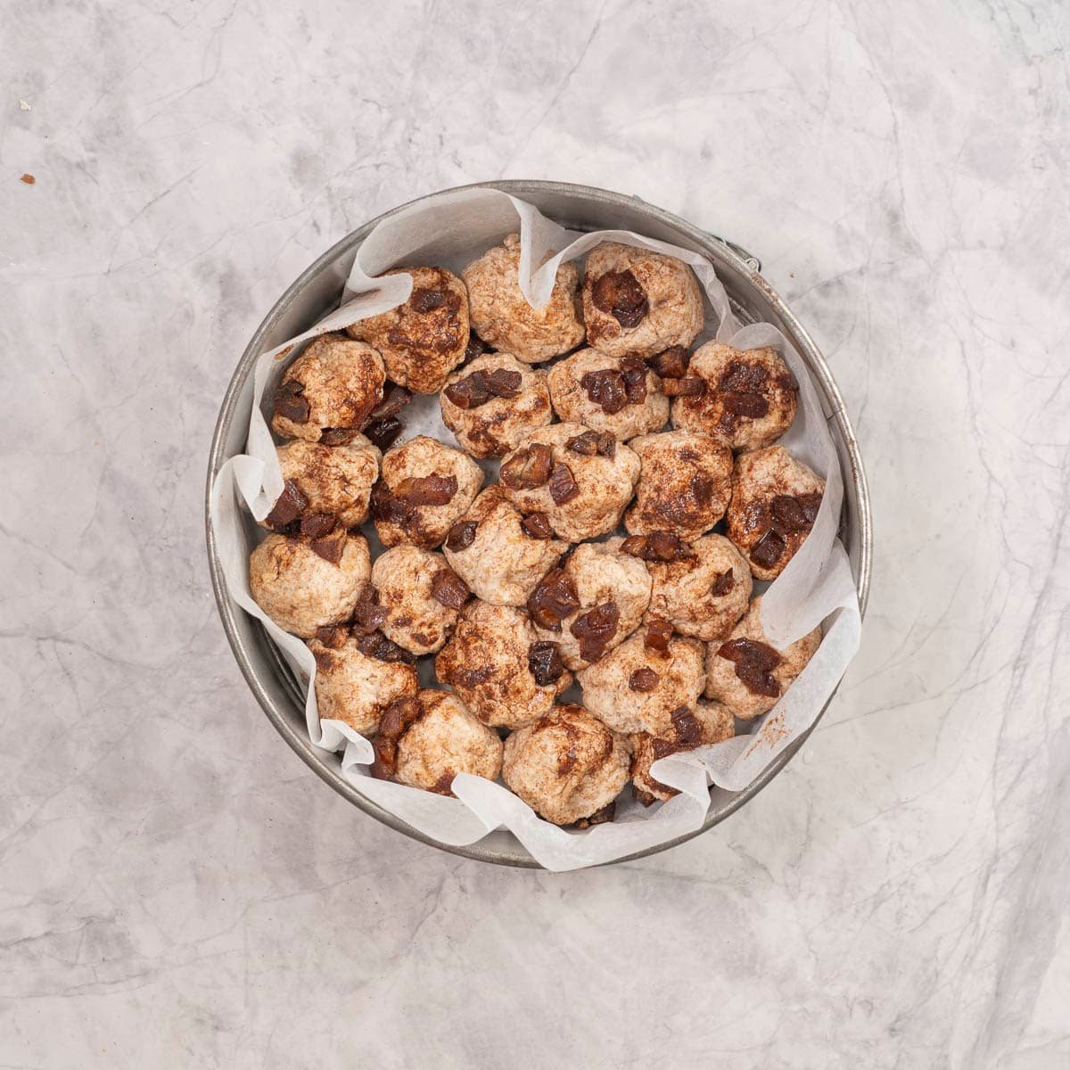 Monkeybread dough balls placed inside a lined metal circle baking dish.