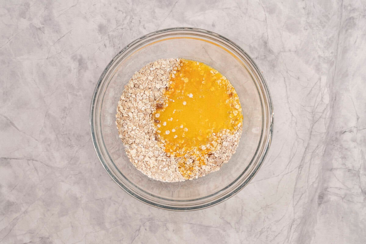 Wet ingredients poured into dry ingredients in glass bowl on benchtop.
