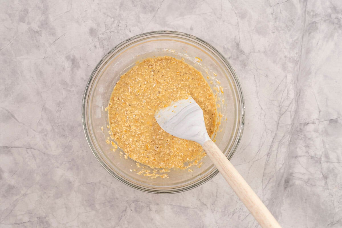 Wet and dry ingredients mixed together in large glass bowl with spatula inside.