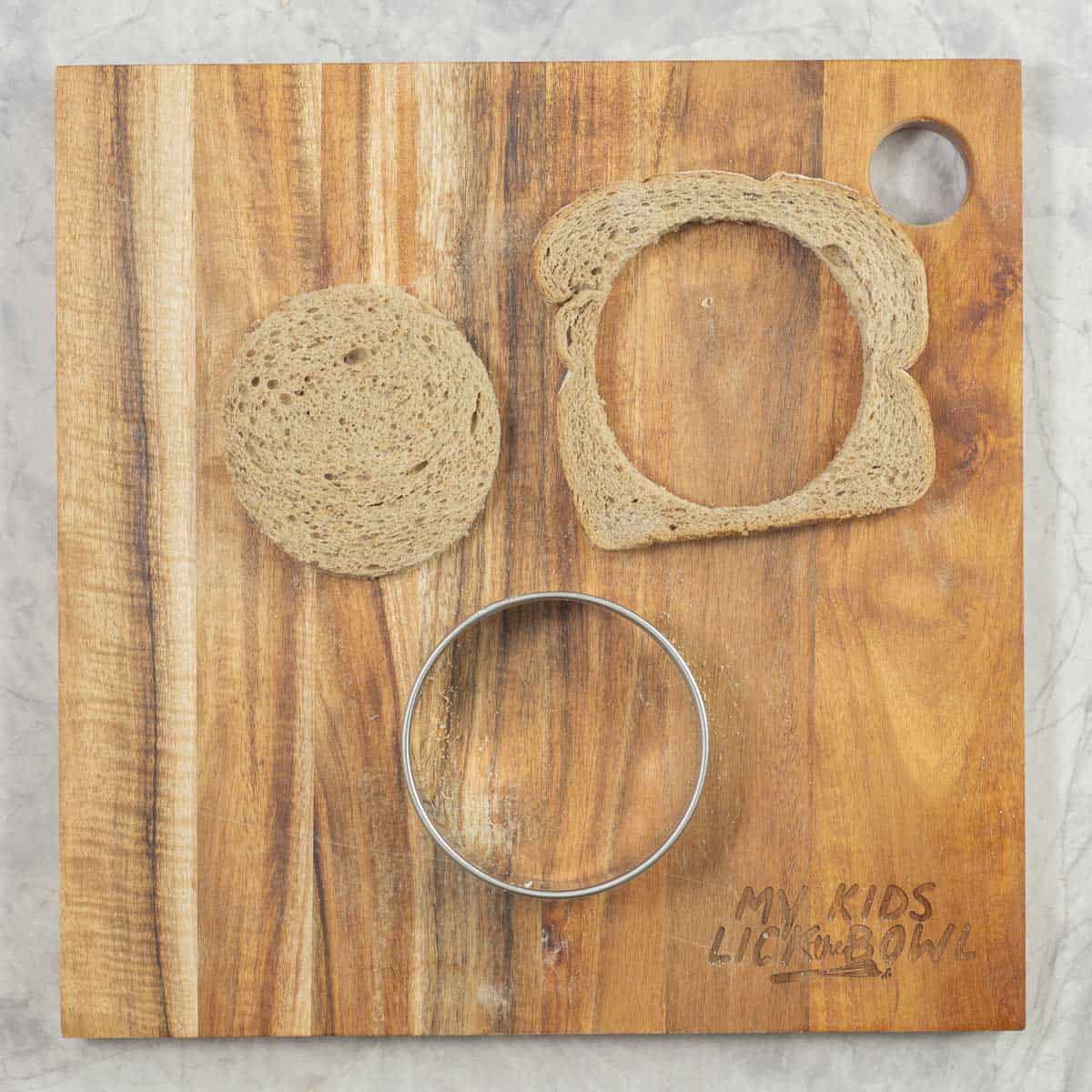 A slice of bread that has been cut into a circle with a cookie cutter, crusts left on the chopping board. 