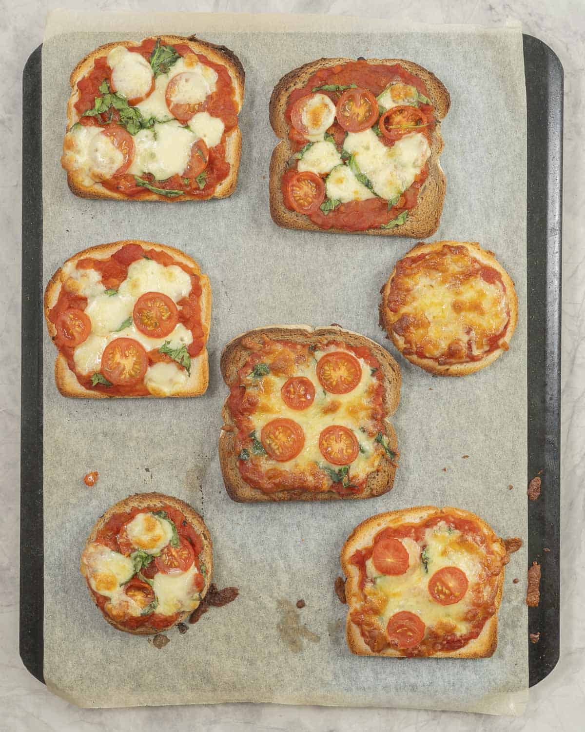 7 golden baked pizza toast on a lined baking tray. 