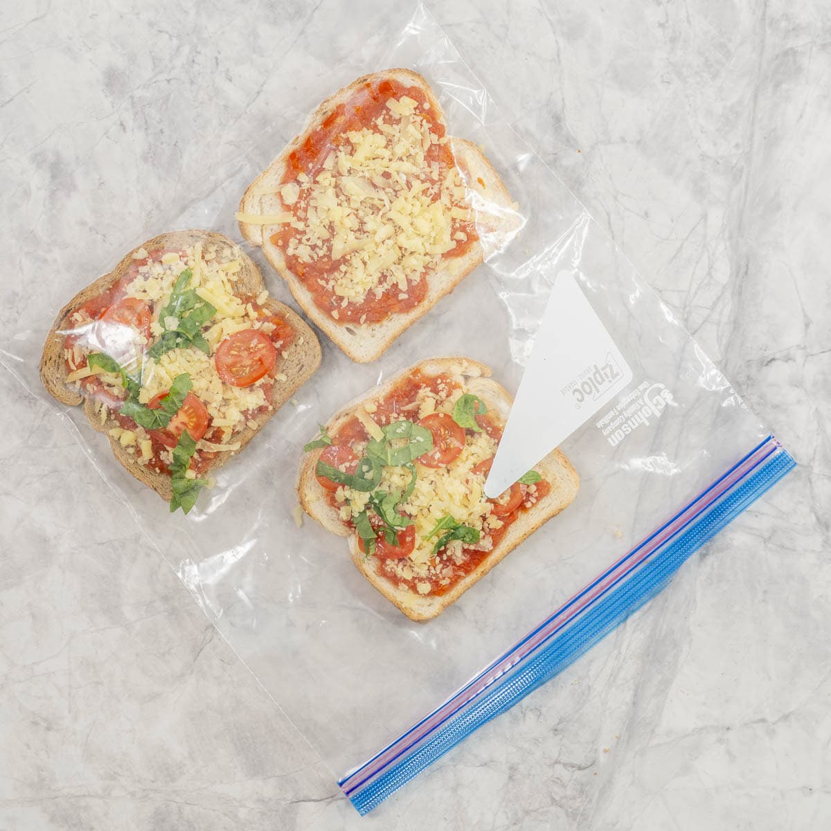 Three prepped pizza toasts lying flat in a zip lock bag ready to go in the freezer. 