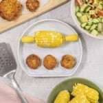 A marble coloured silicone baby plate with half a corn cob (corn handles inserted each end and 3 small fish cakes.