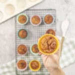 Hand holding a weebix muffin in yellow silicone mold above cooling tray with rest of muffins below.