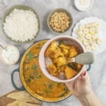 Hand holding toddler silicone plate with baby fork, rice and chicken curry inside. Sides blurred in background on benchtop.
