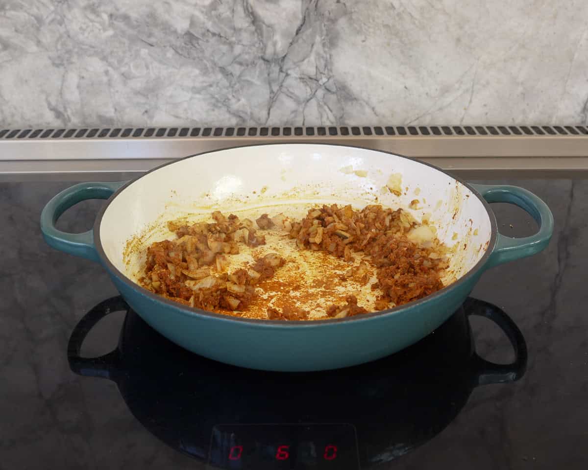 Curry paste mix combined with onion in pan on stove top.