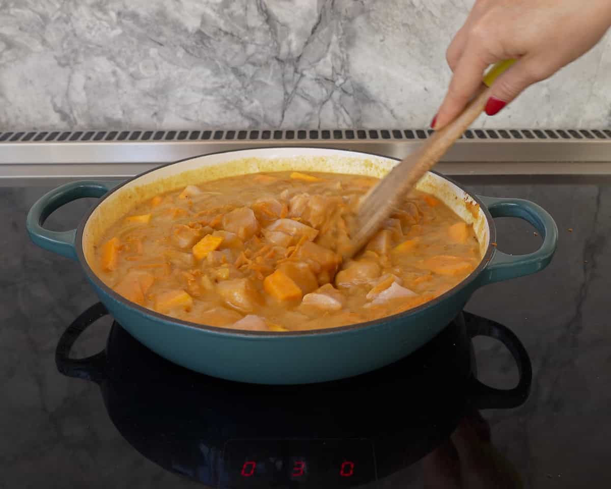 Hand holding a wooden spoon mixing curry ingredients together.