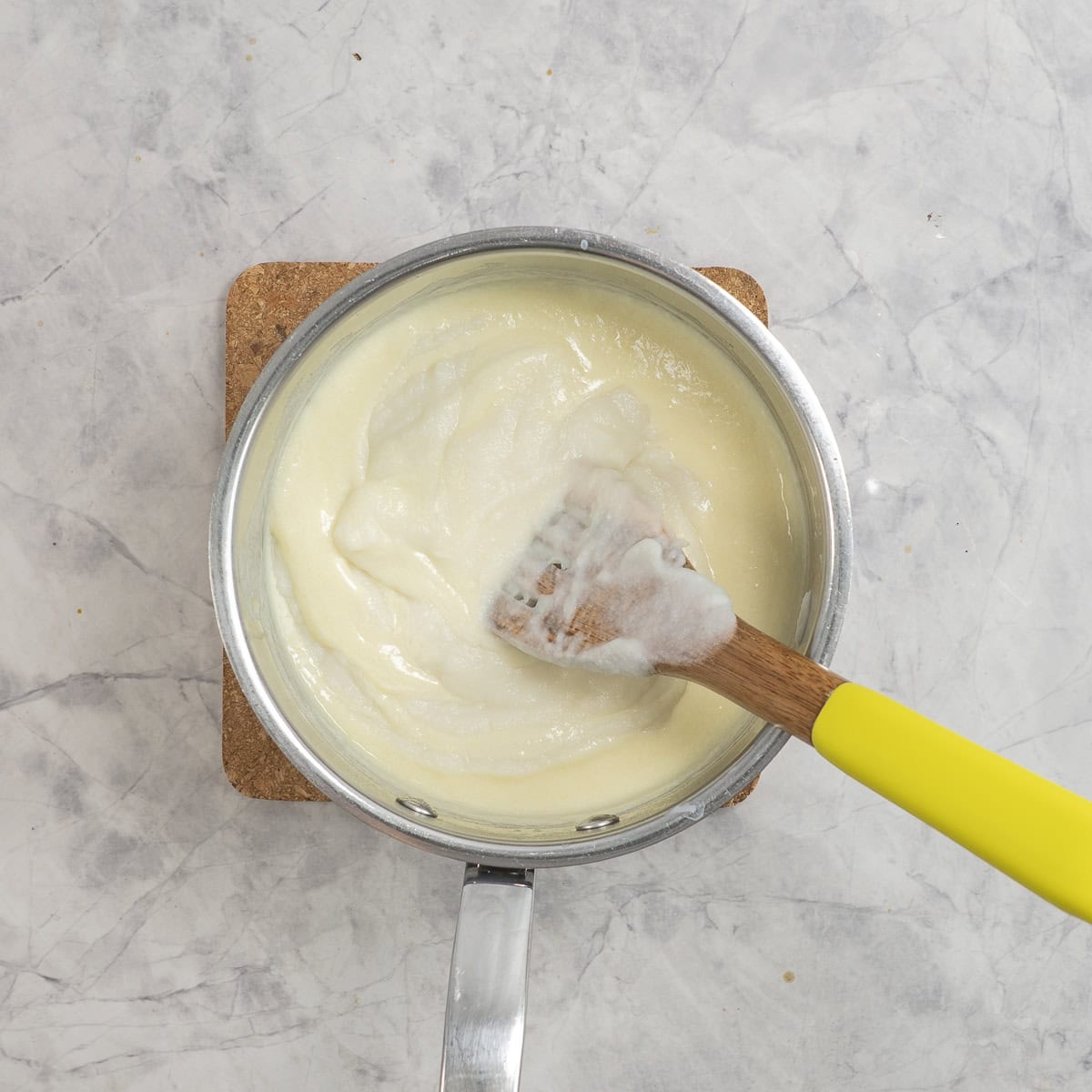 Cauliflower cheese sauce in pot on benchtop with wooden spoon inside.