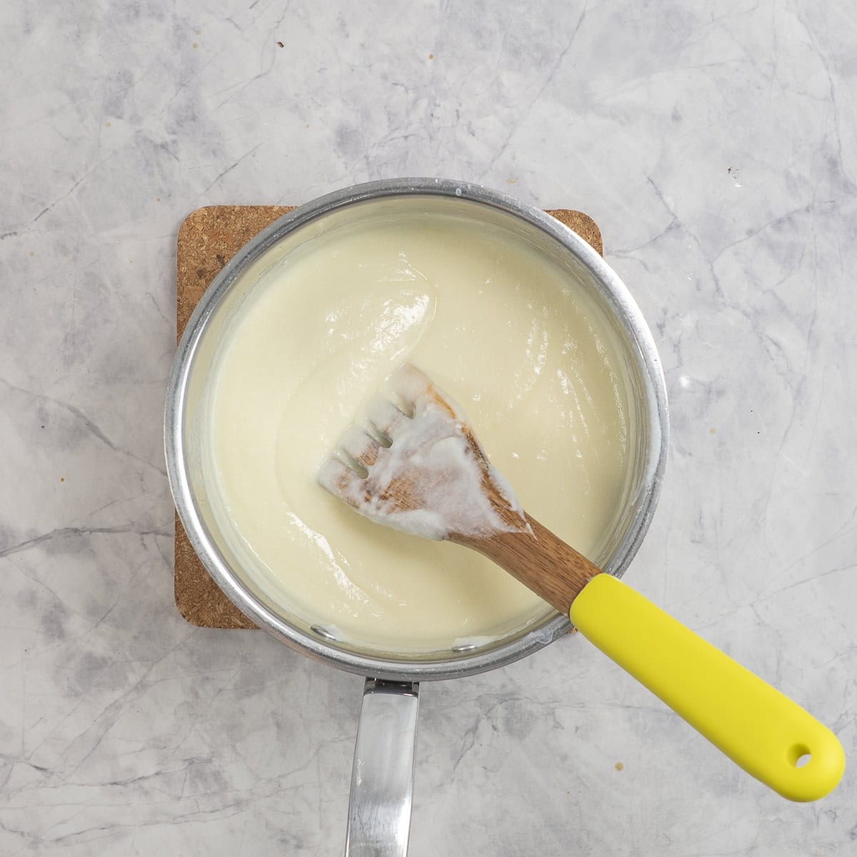 Cauliflower cheese sauce in pot on benchtop with wooden spoon inside.