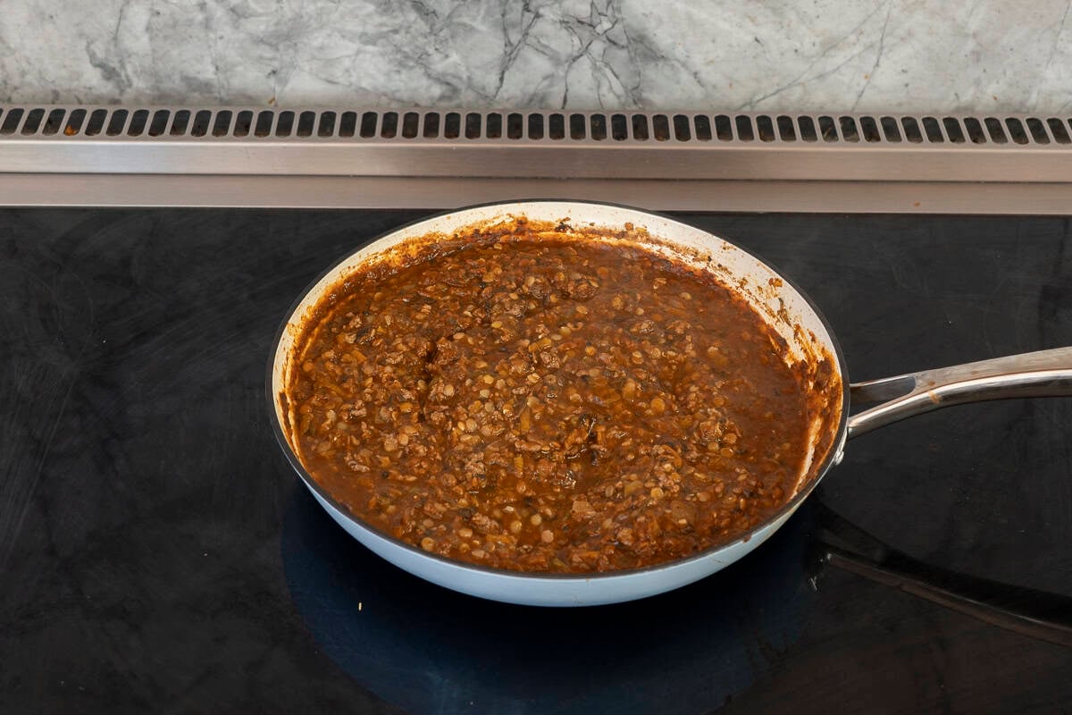 Lentils, spinach and passata sauce added into vegetables and mince in pan.
